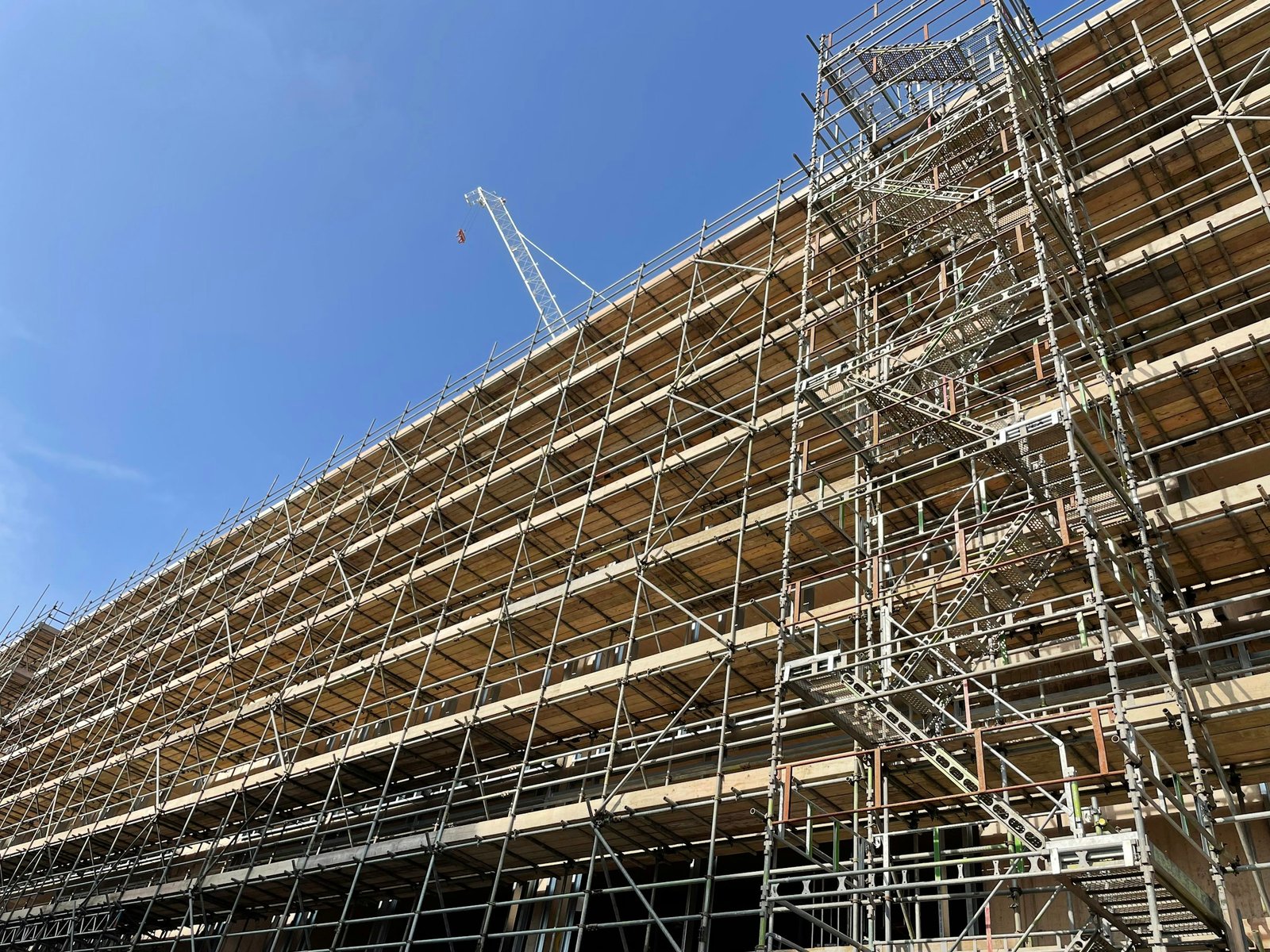 Échafaudages montés sur toute la façade d’un immeuble en construction, grue en arrière-plan
